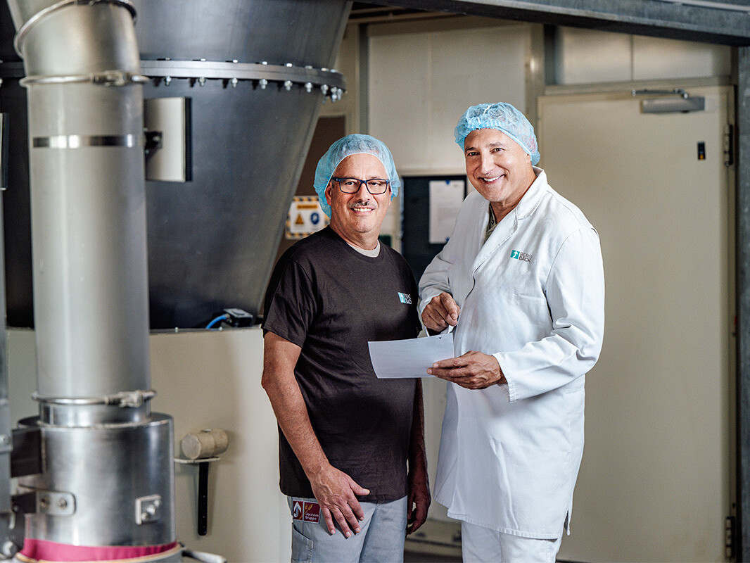Two chefs in hairnets posing in professional commercial kitchen near industrial cooking equipment and vents