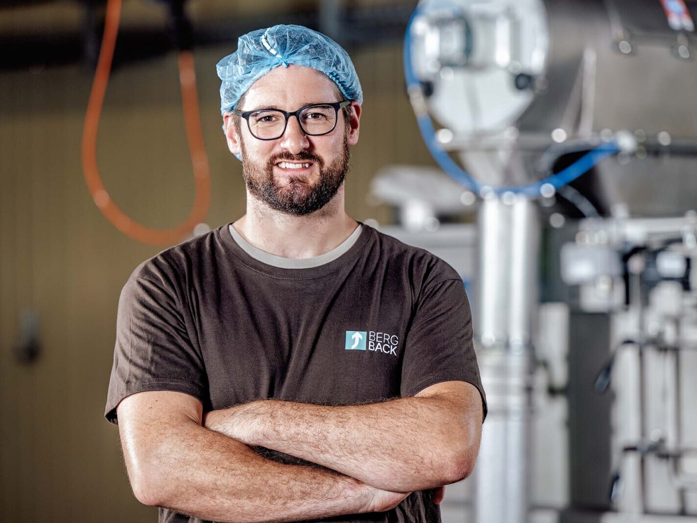 Male industrial engineer wearing hair net and glasses in beverage processing plant with Bergback logo