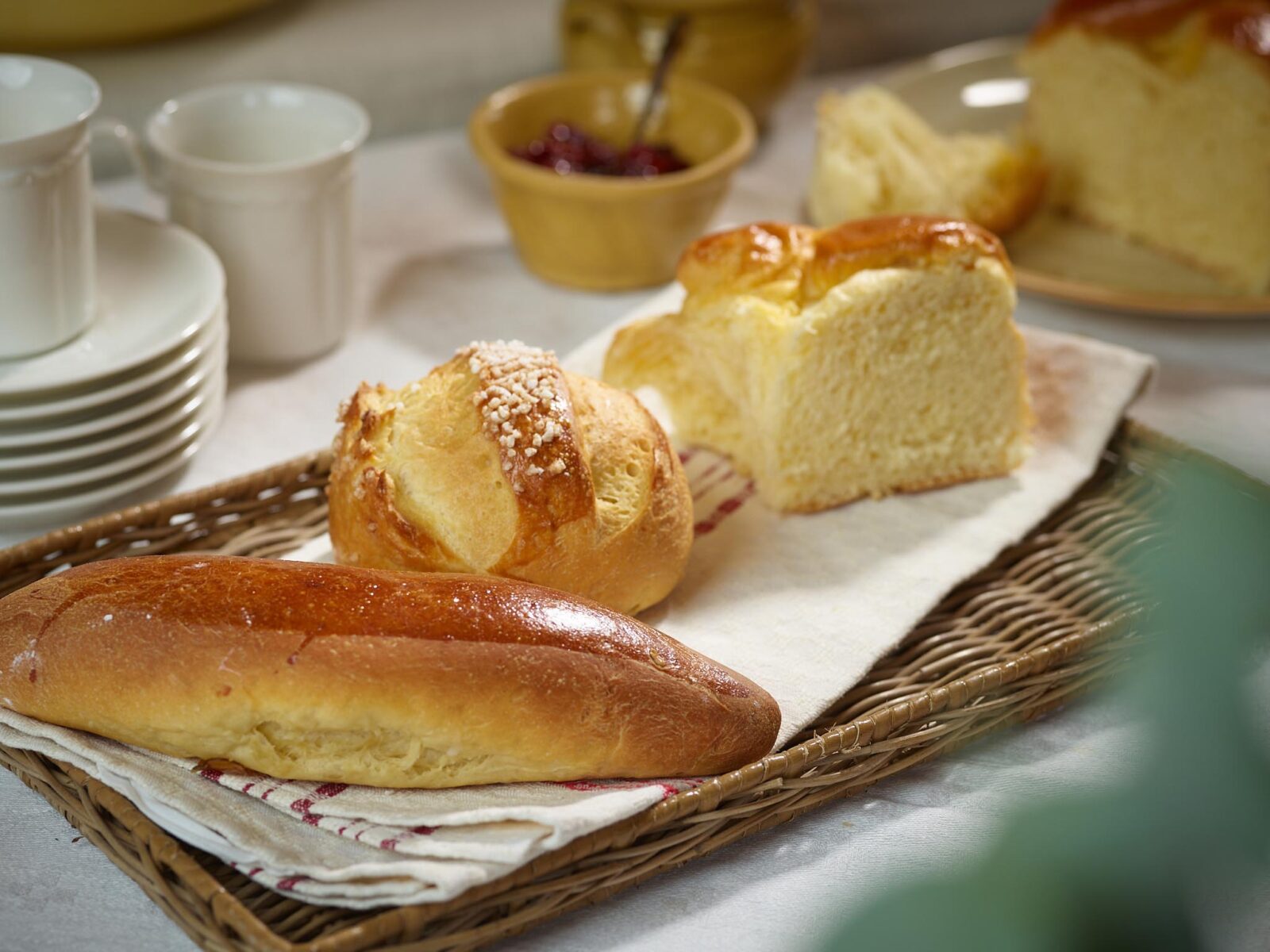 Fresh baked bread rolls and brioche on a serving basket with butter and fruit toppings in background