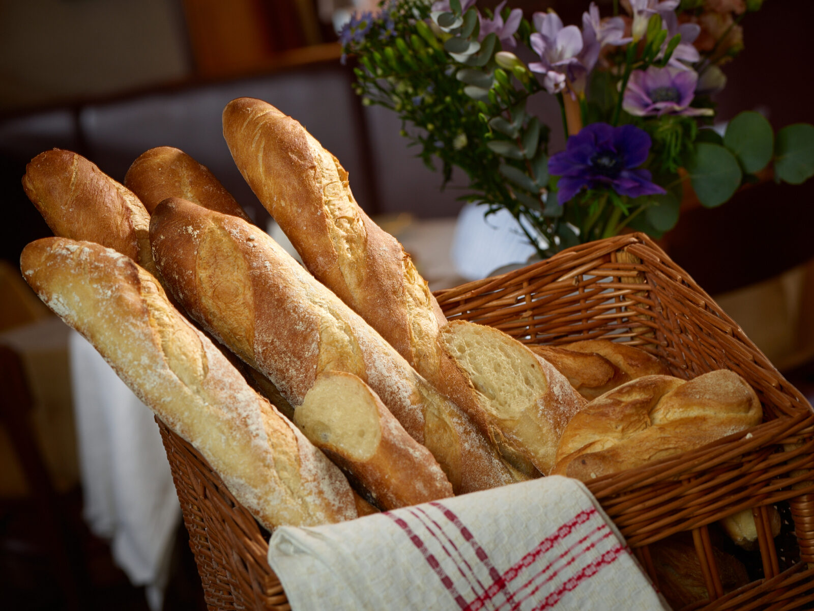 Fresh baguette loaves in a wicker basket with purple and green flowers background in warm light, bakery food photo