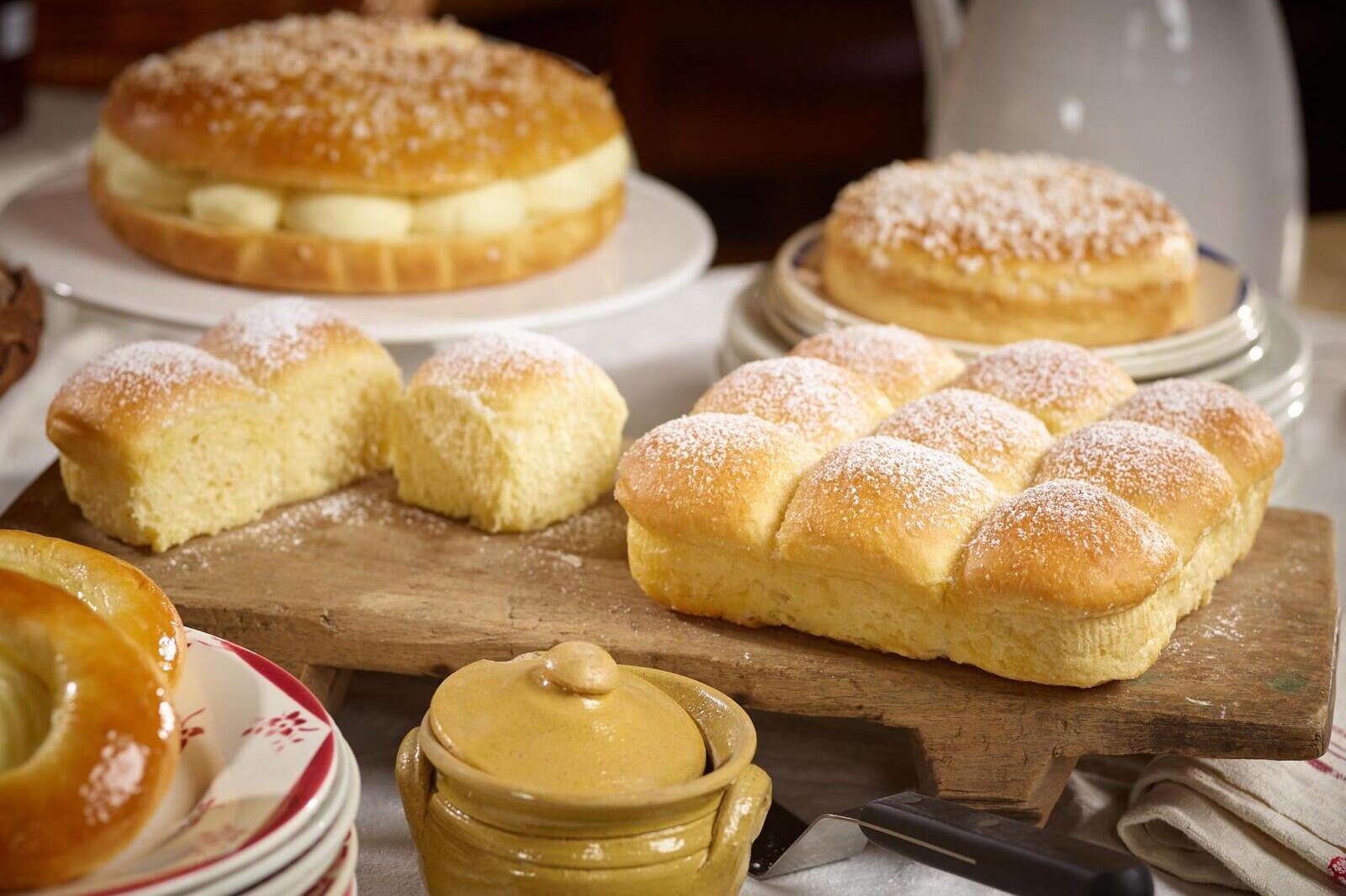 Fresh homemade brioche rolls and pastries dusted with powdered sugar on a wooden board, bakery display