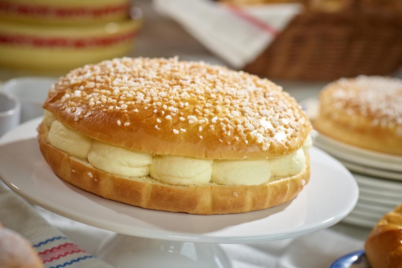 Freshly baked Portuguese custard bread roll with powdered sugar on a plate, close-up in bakery setting