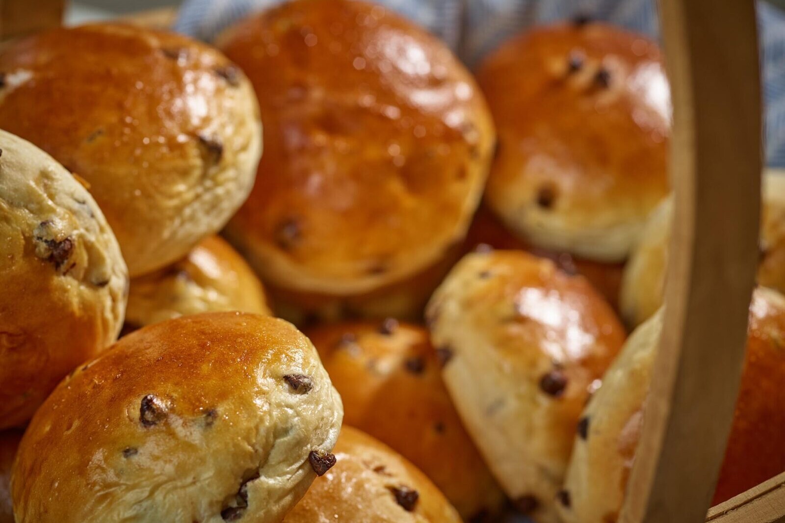 Rustic baked raisin bread rolls in a wooden box, golden brown pastries with dark currants
