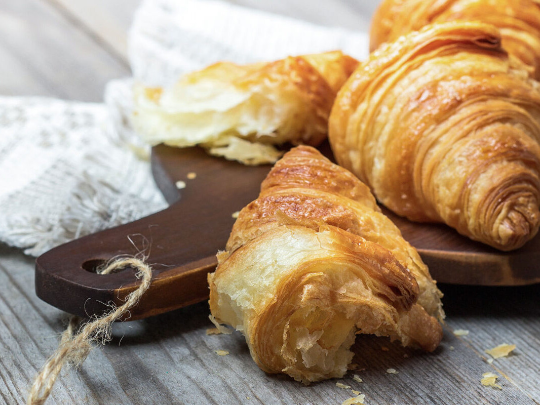 Freshly baked croissants on a wooden board, showcasing flaky layers and golden crust, perfect for breakfast delights.
