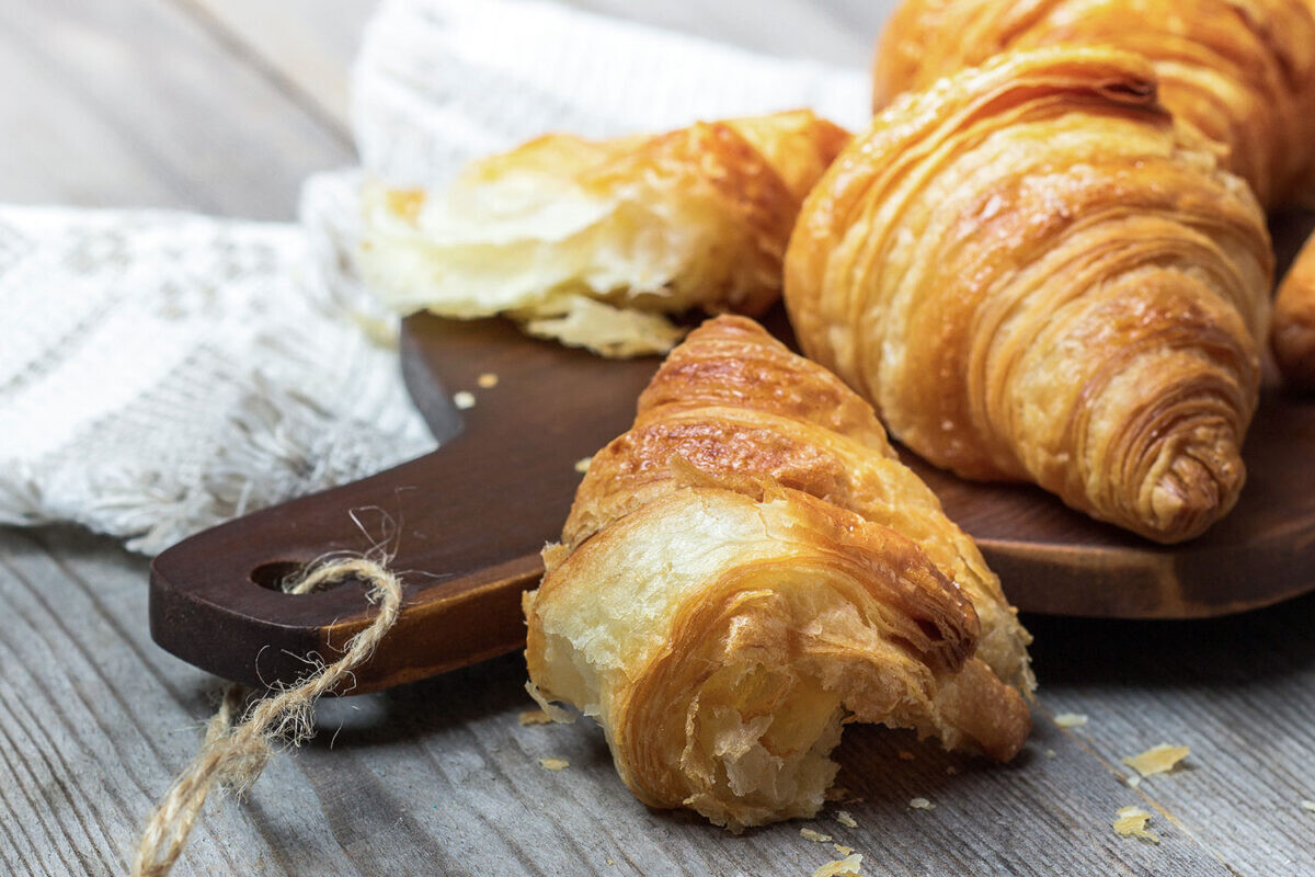 Freshly baked croissants on a wooden board, showcasing flaky layers and golden crust, perfect for breakfast delights.