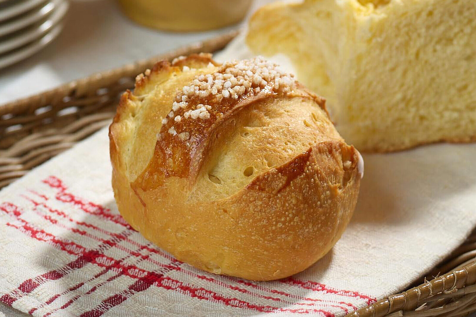 Rustic golden bread roll with flaky salt, served on a linen cloth and wicker basket background.