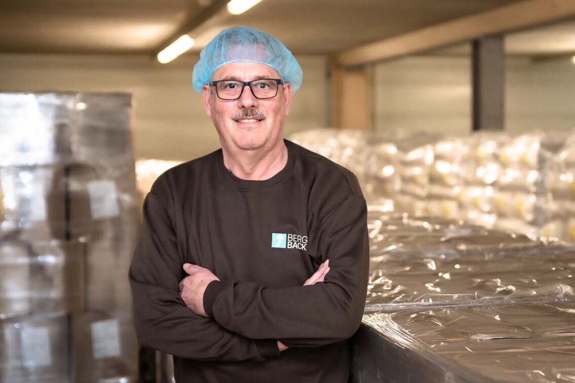 Male chef wearing hairnet and glasses standing in a food processing facility, arms crossed, Berg Back workwear.