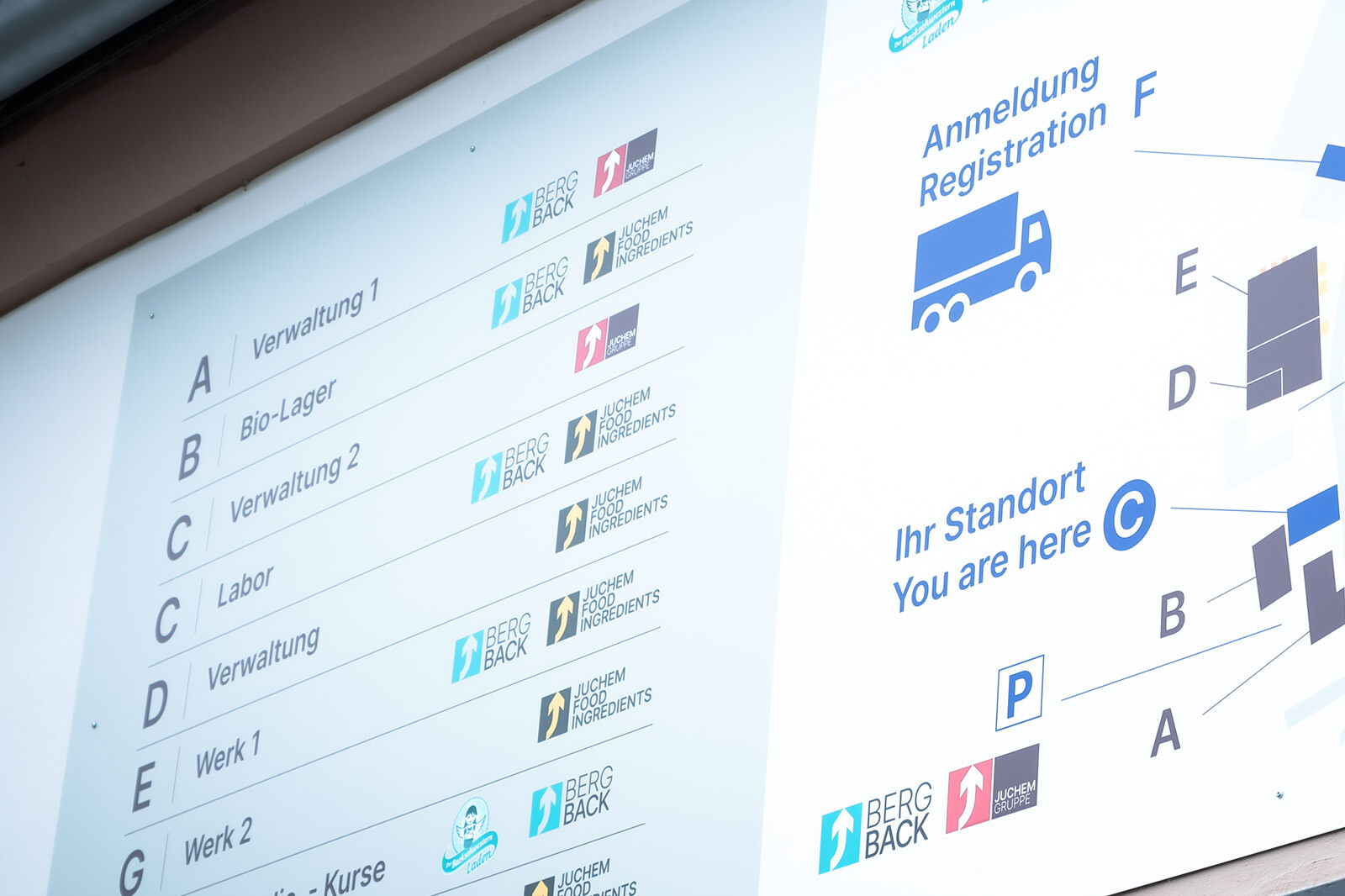 Photo of digital screen showing warehouse process steps and “Anmeldung Registrierung” at JUCHHEm/BERG BACK event