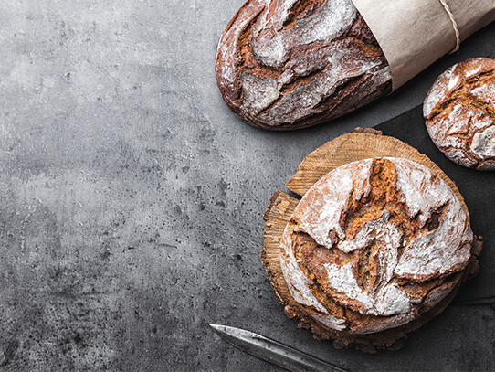 Rustic sourdough bread loaf and rolls with flour on parchment, rustic knife on dark background, copy space