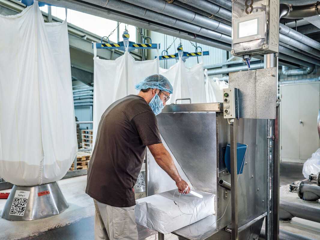 Worker in hairnet and lab coat packaging products beside industrial machinery in clean production facility