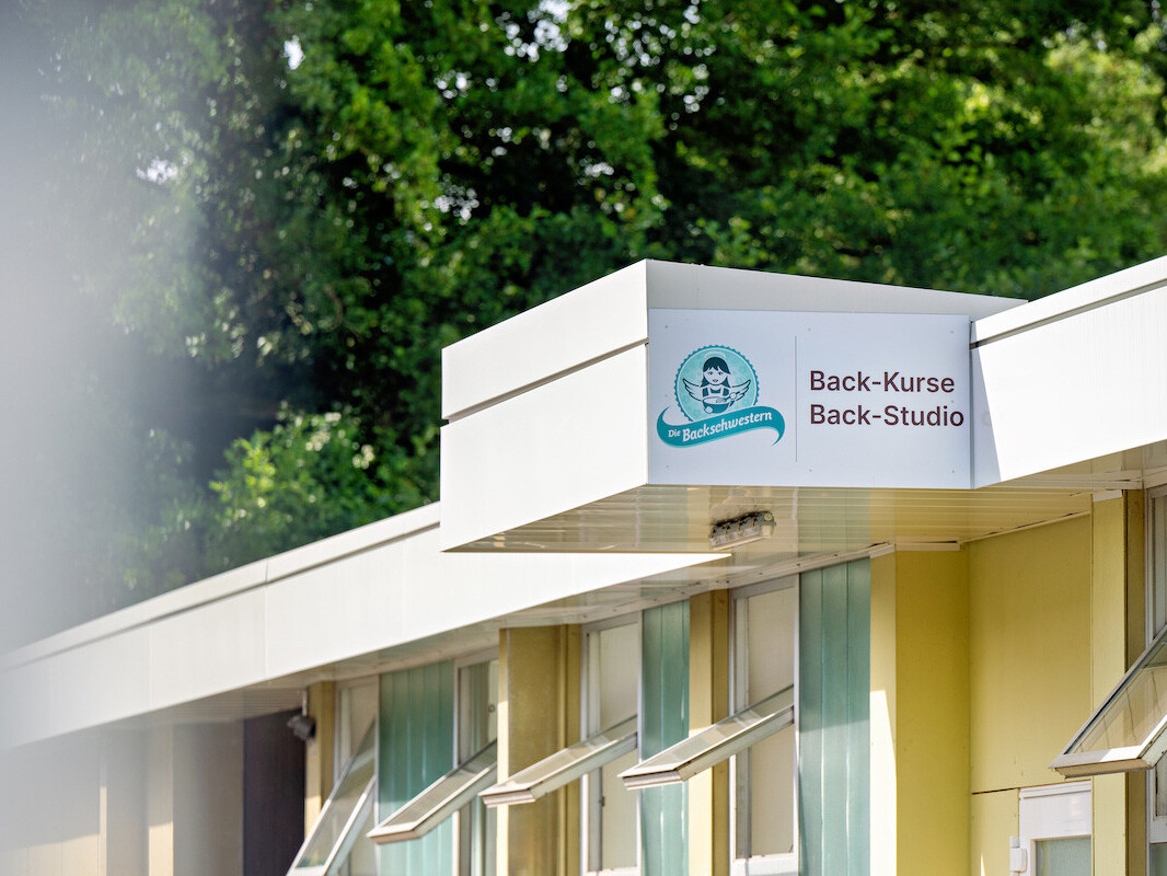 Die Backschwestern back course studio sign on modern building facade with trees background