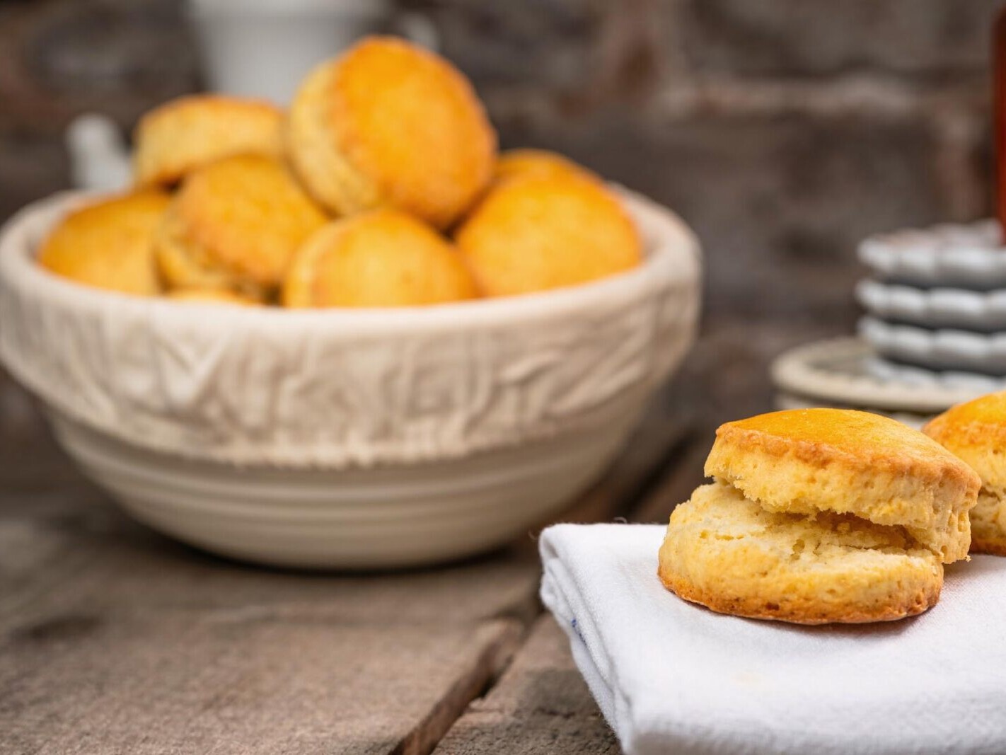 Fresh baked cornbread biscuits in a bowl, with sliced pieces on a cloth, rustic kitchen background