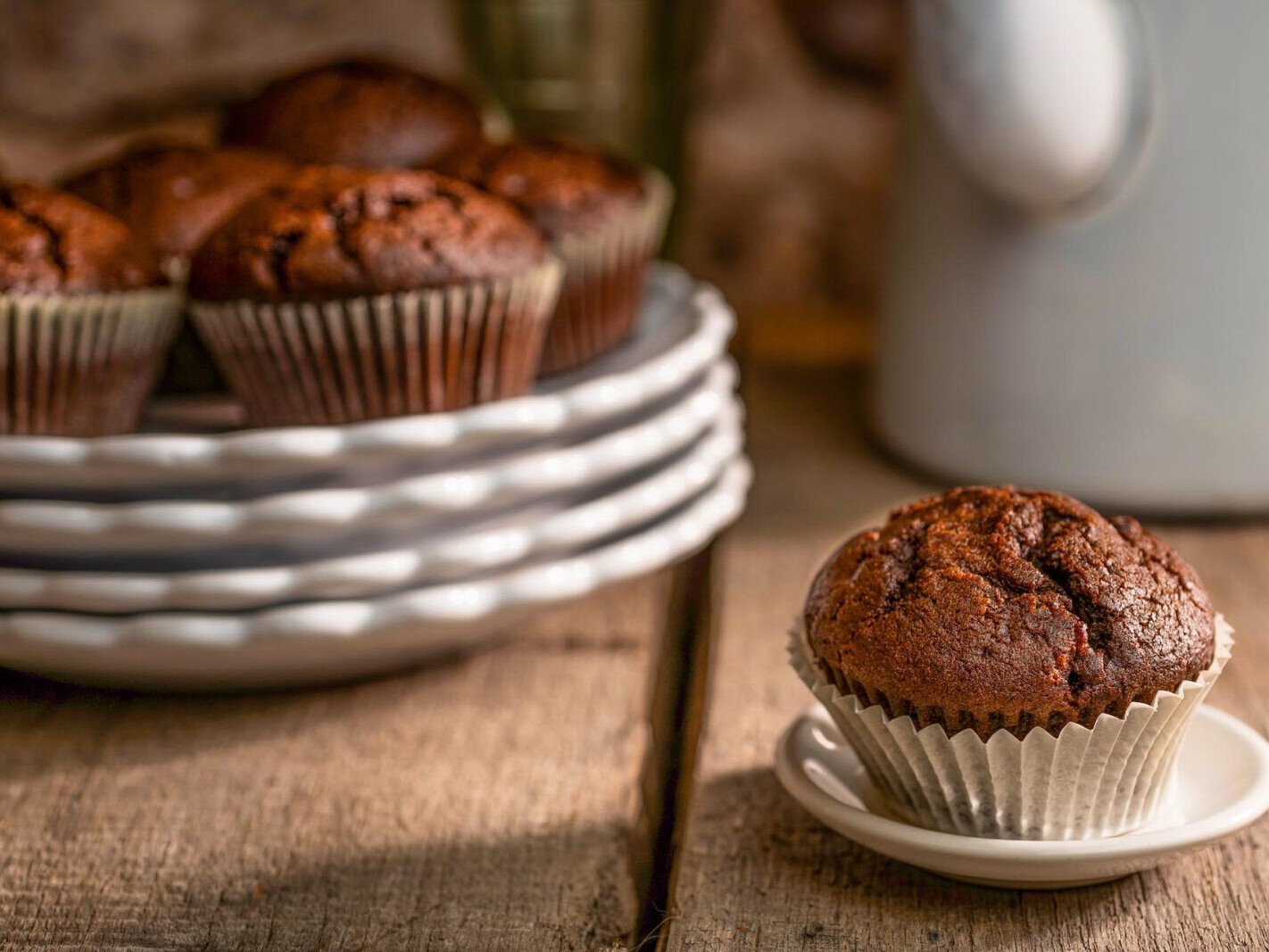 Fresh baked chocolate muffins on a wooden table with coffee cup background, warm bakery-style photo