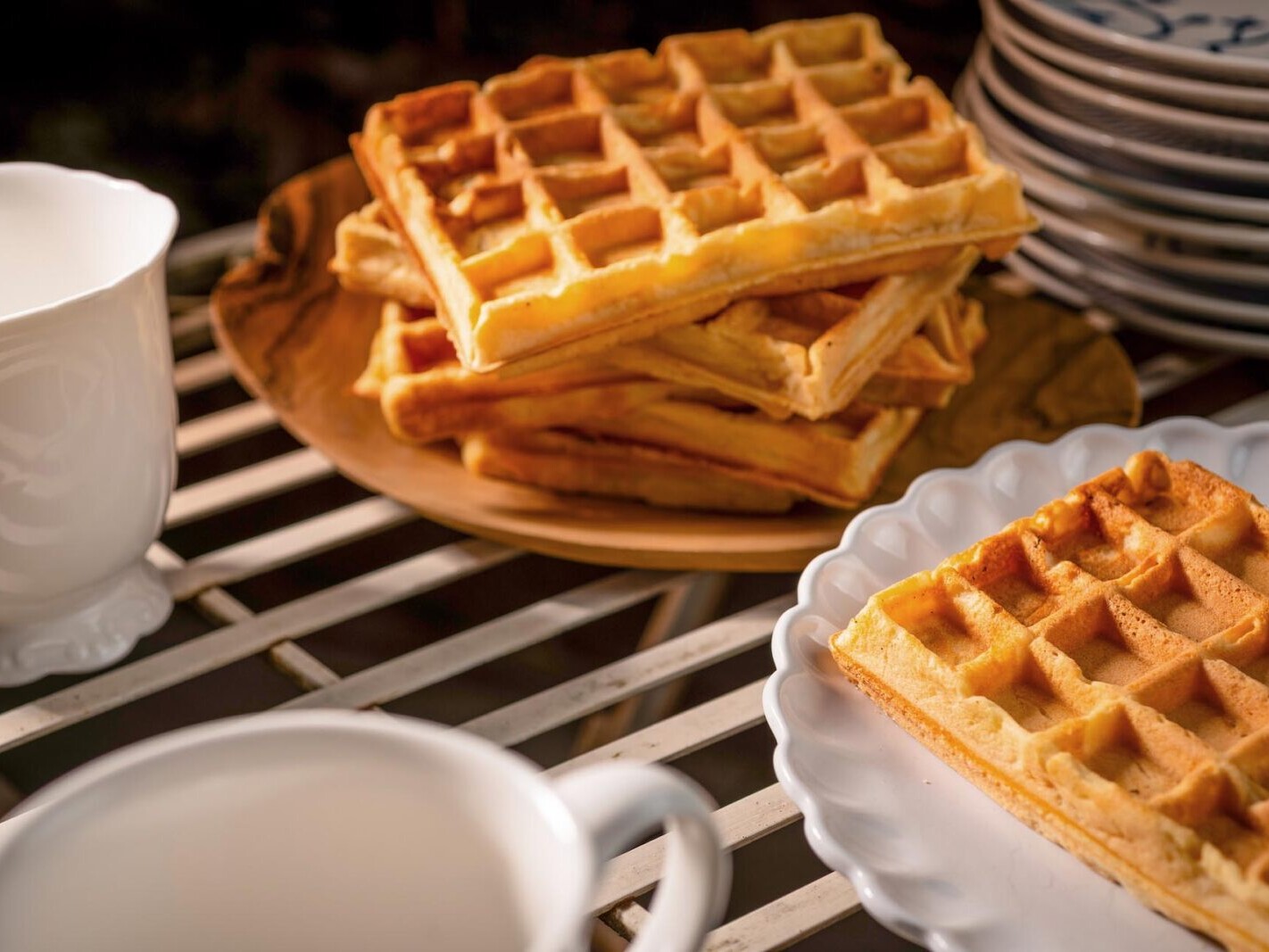 Golden Belgian waffles stacked on a tray with syrup and plates on a grill—fresh breakfast food photo