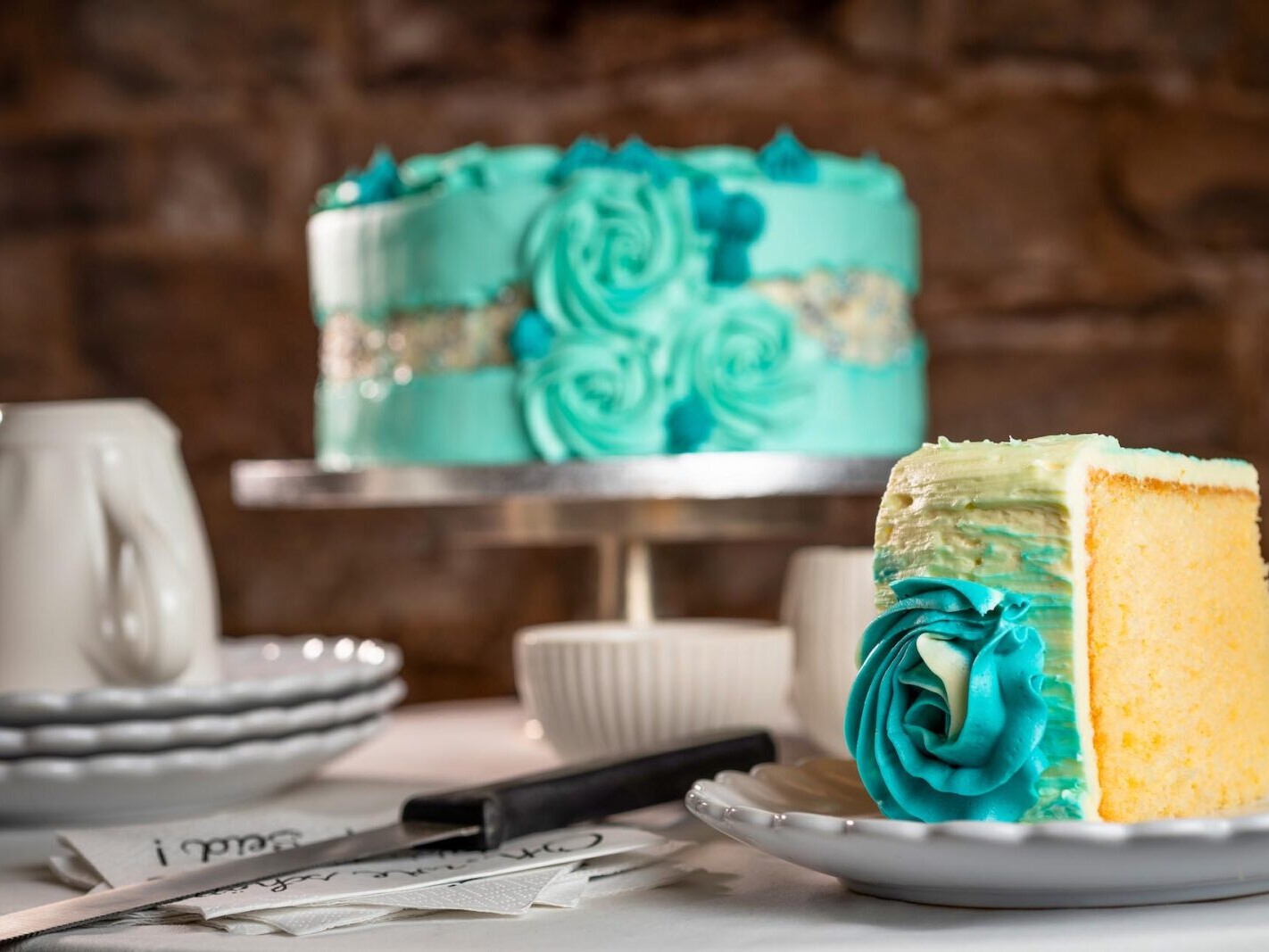 Turquoise-frosted cake slice with teal buttercream rose design on a table, celebration dessert background