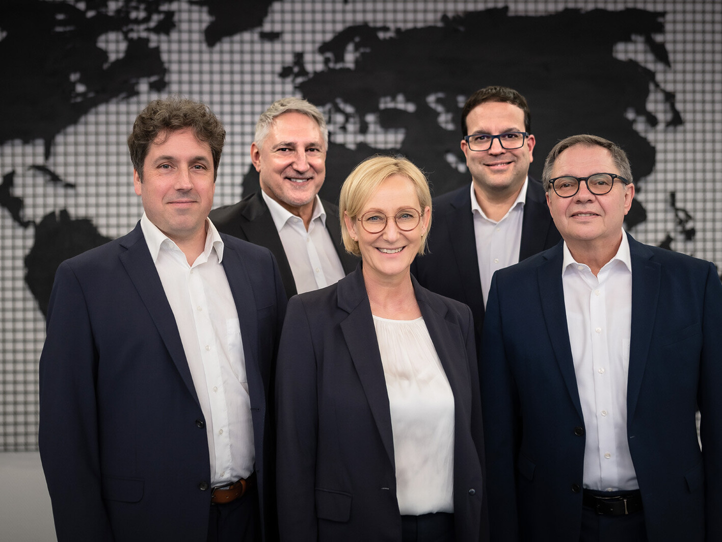 Business team portrait of five professionals in suits with a world map backdrop, corporate group photo
