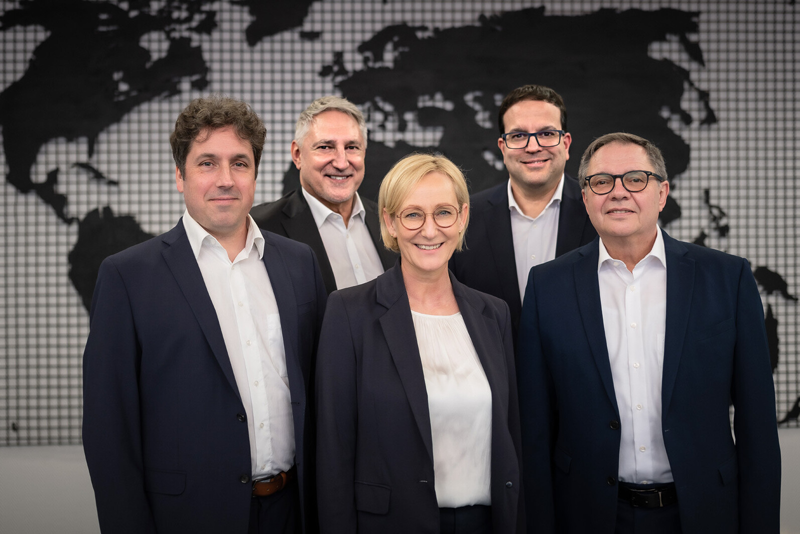 Business team portrait of five professionals in suits with a world map backdrop, corporate group photo