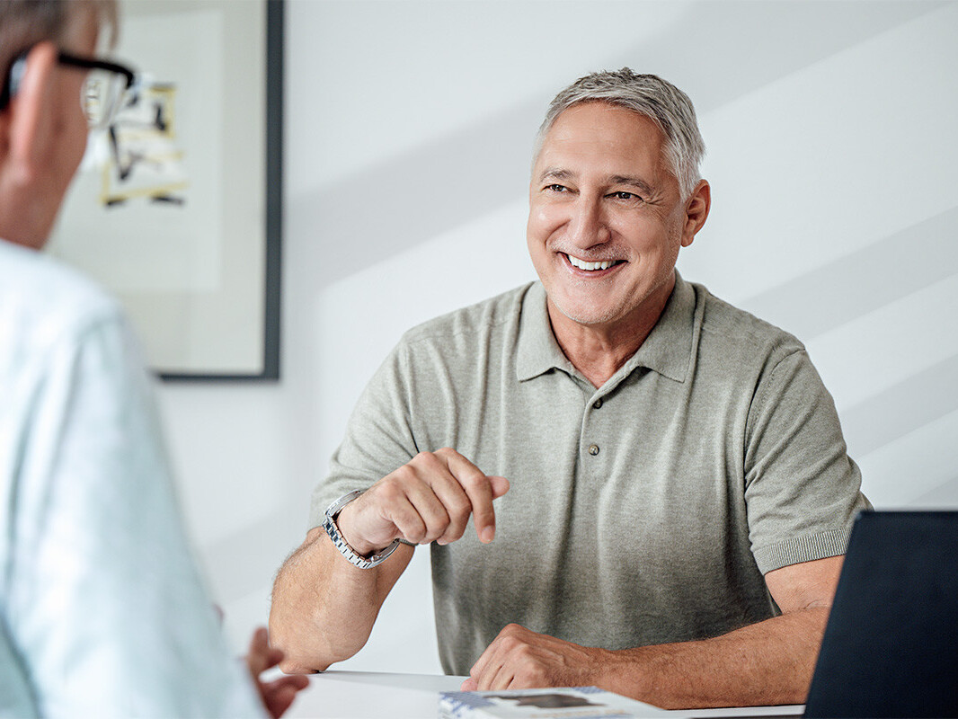 Smiling businessman in casual meeting, using laptop and notes at a desk.
