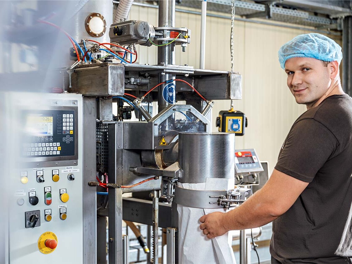 Factory worker operating industrial packaging machine with a control panel.