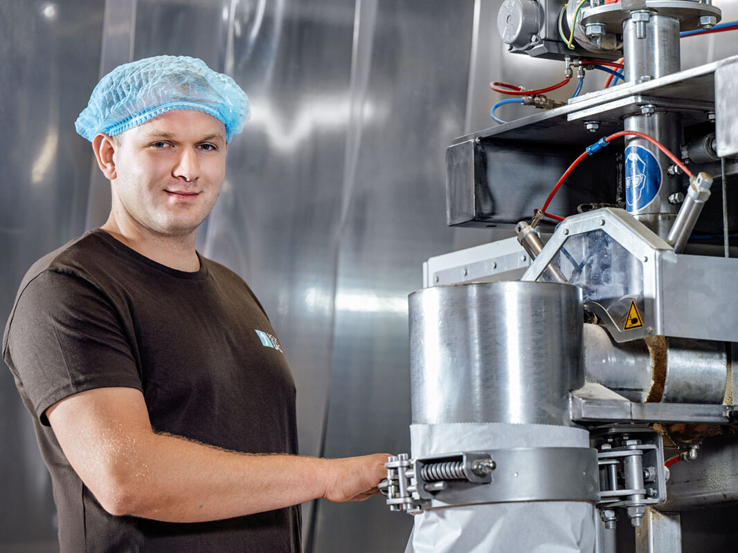 Factory worker operates food processing machine wearing a hairnet, ensuring safety and hygiene standards.